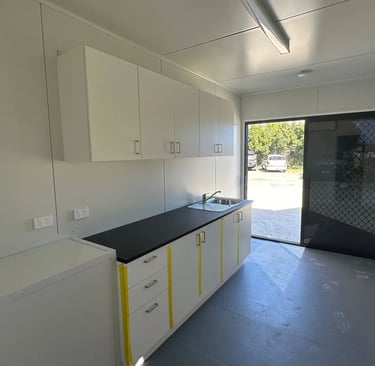 Modern portable cabin kitchenette with white cabinets, black countertop, and stainless steel sink.