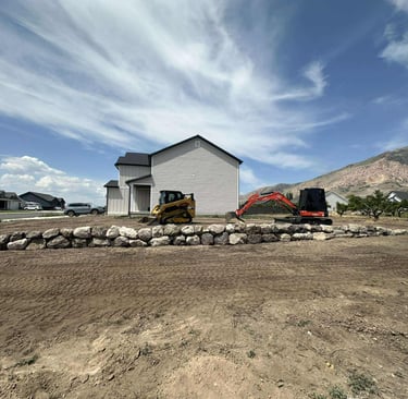 Boulder retaining wall with skid steer and mini excavator sitting idle