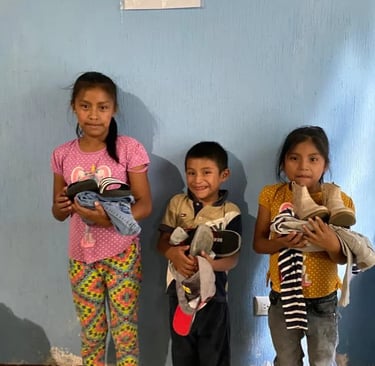 Three young children smiling while holding donated shoes and clothes from a charity donation center.