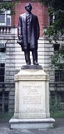 Bronze statue of Henry Cabot Lodge standing on a stone pedestal outside a brick building.