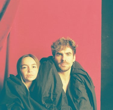 A man and woman posing wrapped in black fabric against a vibrant red backdrop.
