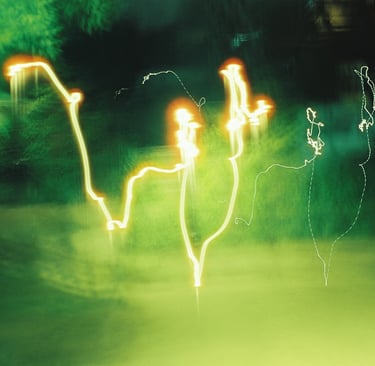 Abstract long exposure photography featuring golden light trails against a blurry green nature background.