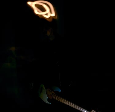 Musician playing a light blue bass guitar in the dark with orange light painting trails.