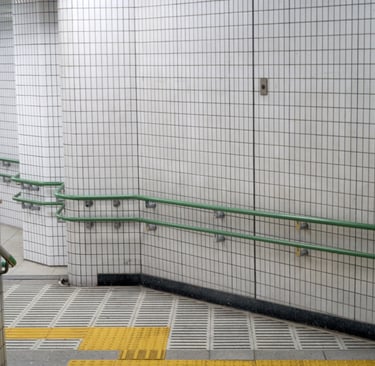 Subway station ramp with white tiles, green metal handrails, and yellow tactile paving for accessibility.
