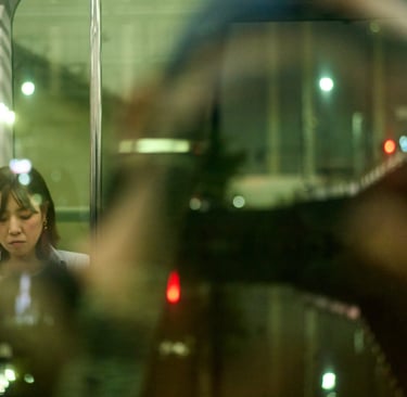Candid shot of a woman on a Tokyo train at night reflecting in the window.