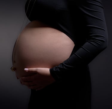 Maternity photo of a pregnant woman in a black dress holding her baby bump against a dark background.