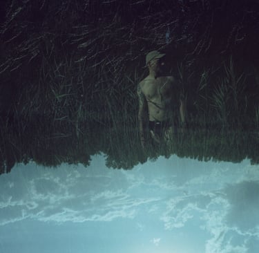 Surreal double exposure of a man in tall grass merged with an upside-down blue sky and clouds.