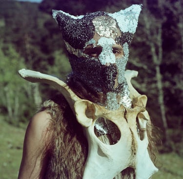 A person wearing a beaded animal mask and a large bone collar in a shamanic ritual style costume.