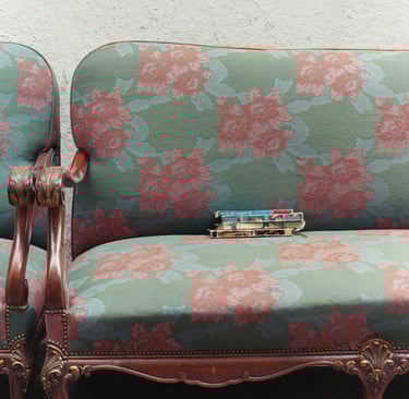 Vintage floral tapestry settee with carved wood frame featuring a stack of antique books on the seat cushion.
