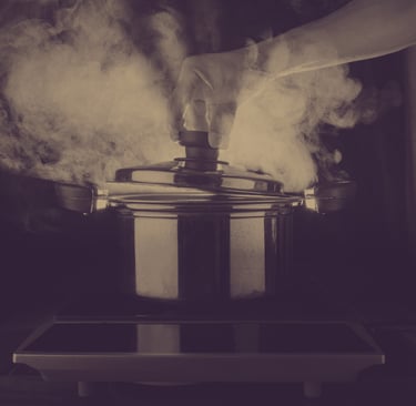 Steam rising from a stainless steel cooking pot as a hand lifts the lid on an electric stovetop.
