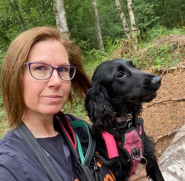 A dog trainer and her black cocker spaniel sit together on a log during a walk