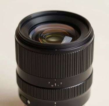 Minimalist macro photography of a photography lens reflecting soft, ambient light in a studio setting. The composition is artistic and high-end, with deep shadows and soft highlights of #FDFBF7. Elegant and professional atmosphere.