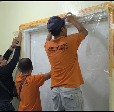 Professional exterminators from Jansen Pest Control sealing a door with plastic for termite fumigation.