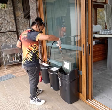 Professional pest control technician spraying disinfectant into outdoor trash cans for sanitation.
