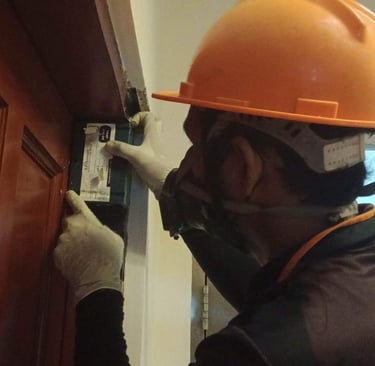 A pest control professional wearing a hard hat and mask inspects a wooden door frame for termite damage.