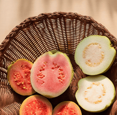 Fresh pink and white guava slices arranged in a rustic wicker basket on a sunny table.