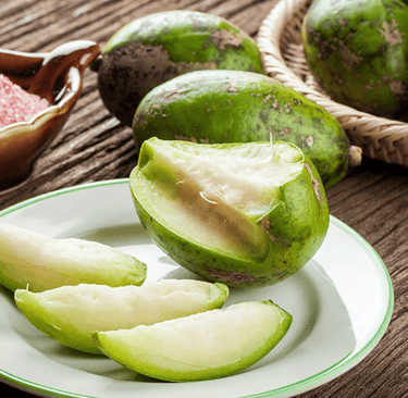 Slices of fresh June Plum fruit served on a white plate with pink salt.