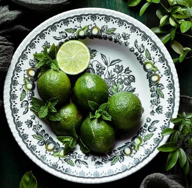 Fresh whole limes and mint leaves on a vintage floral patterned ceramic plate.