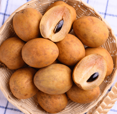 Fresh ripe sapodilla fruit and sliced chikoo with seeds in a wicker basket.