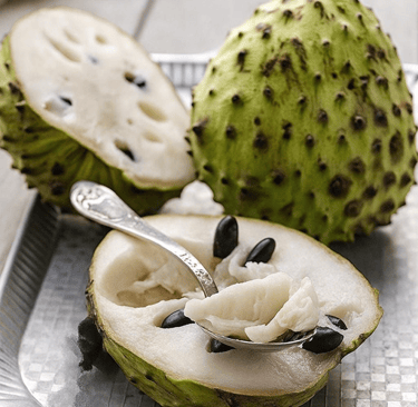 Fresh soursop fruit sliced open on a tray with white pulp and black seeds.