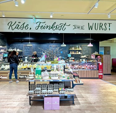 A gourmet deli counter featuring cheese, charcuterie, and specialty sausages inside a German grocery store.