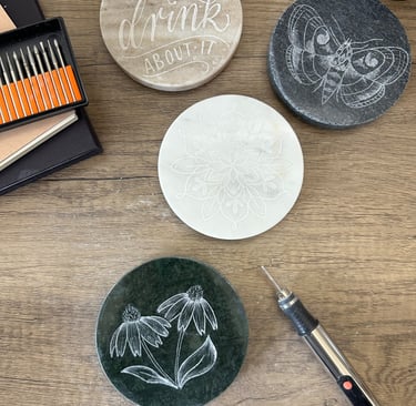 Custom engraved stone coasters with floral and butterfly designs made using a rotary diamond burr tool.