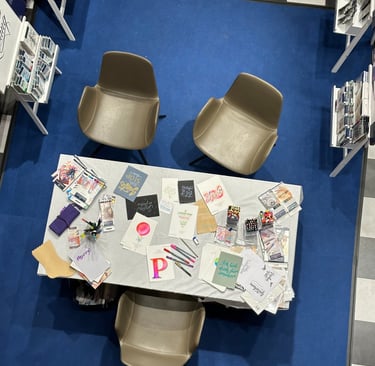 Top-down view of a stationery workshop table with modern chairs, calligraphy cards, and colorful pens.