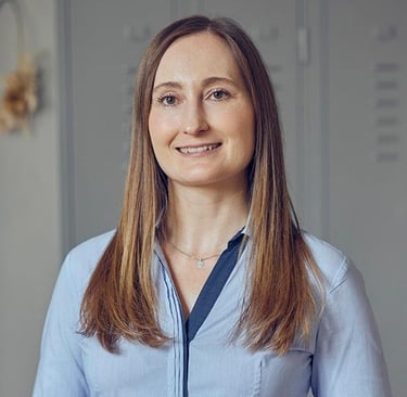 Professional portrait of a smiling woman with long brown hair wearing a light blue button-down shirt.