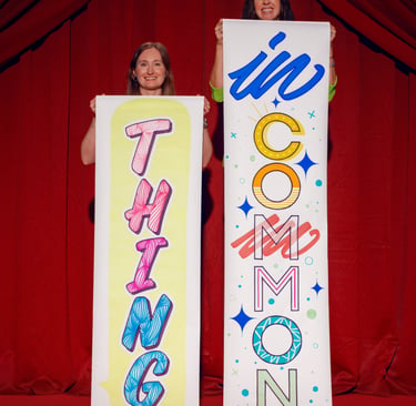 Two women holding vertical banners reading 'Thing' and 'In Common' against red theater curtains.