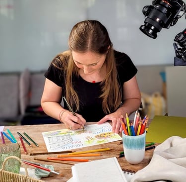 An artist drawing a Croatia travel illustration with colored pencils while being filmed by a professional camera.
