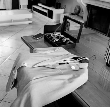 Photo en noir et blanc d'un blazer pour homme et d'un coffret de montre de luxe posés sur une table 