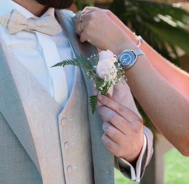 Une femme attache une boutonnière de rose rose au costume de mariage en lin gris clair du marié.