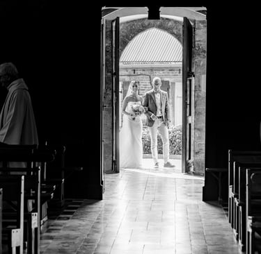 Photo de mariage en noir et blanc d'une mariée et d'un marié entrant dans une chapelle d'église par 