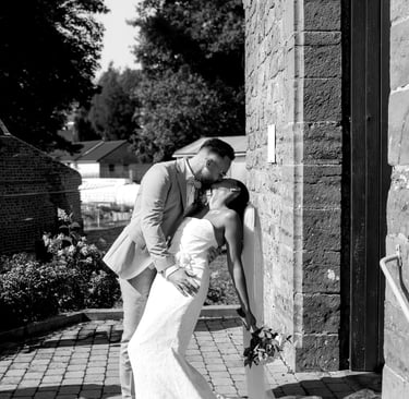 Photo en noir et blanc d'un marié embrassant sa femme devant une Église