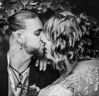 Une photo de mariage en noir et blanc montrant les mariés échangeant un baiser intime en extérieur.