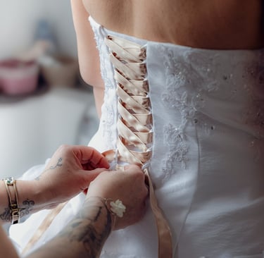 Gros plan sur une mariée se faisant lacer sa robe de mariée en dentelle blanche avec un ruban de cor