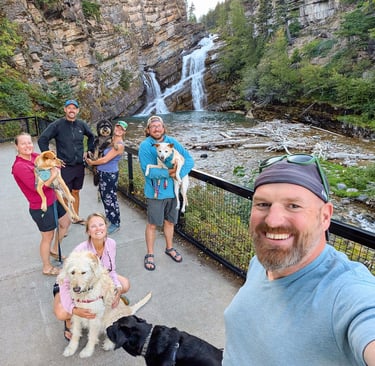 Travel group with their dogs smiling at Cameron Falls waterfall in Waterton, Alberta.