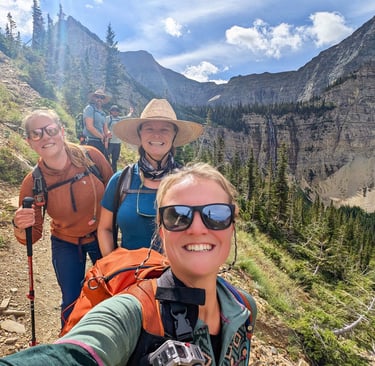 Hikers smiling on the Crypt Lake Trail with Crypt Falls visible in the background in Waterton Lakes