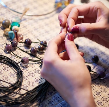 Joyera insetando cuentas de vidrio hechas a mano en un cordón negro para crear joyas personalizadas.