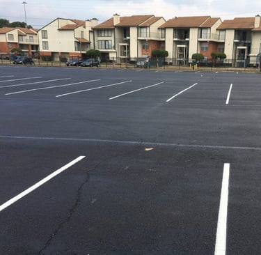 Freshly paved asphalt parking lot with white stripes in front of an apartment complex.