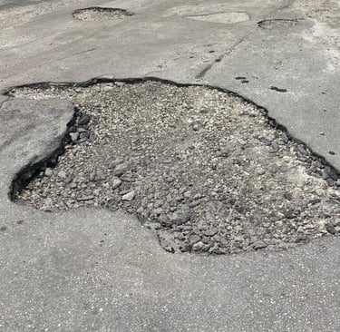 Large deep pothole in damaged asphalt road requiring professional pavement repair services.