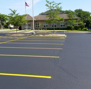 Freshly paved and sealcoated asphalt parking lot with bright yellow striping in front of a commercial office building.