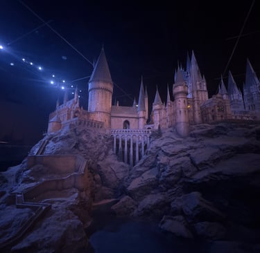 Detailed scale model of Hogwarts Castle with stone towers and bridges under dramatic blue lighting.