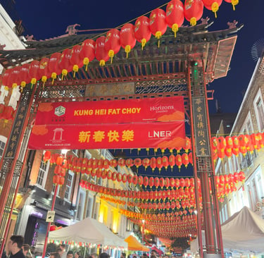Crowded London Chinatown gate decorated with red lanterns and banners for Chinese New Year celebrations.