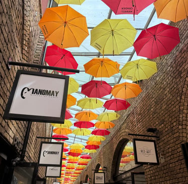 Colorful umbrellas hanging over a brick alleyway in London's Camden Market with shop signs.