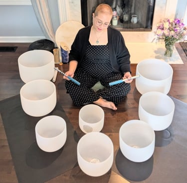 Cricia sits in the floor surrounded by white crystal singing bowls for a sound healing session.