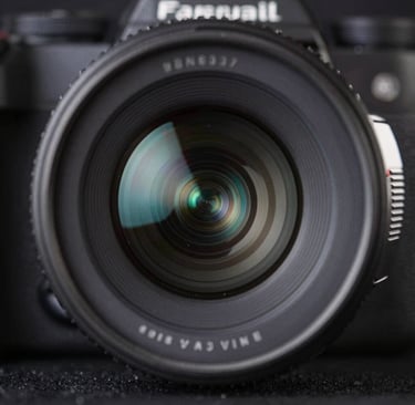 A macro photograph of professional camera equipment, focusing on the precision-engineered glass of a lens reflecting soft pale steel blue light against a deep rich obsidian background.