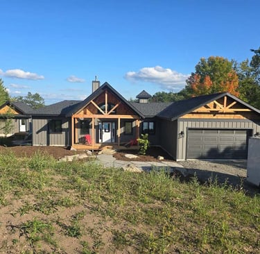 Modern rustic grey farmhouse with cedar wood accents, front porch, and garage under a blue sky.