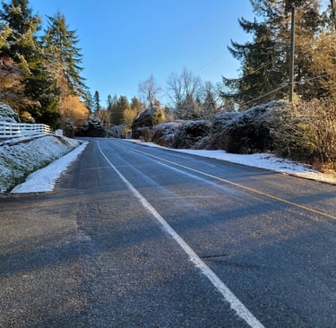 a road with snow on both sides with a white fence and bushes