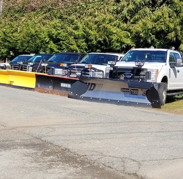 a picture of a street with 5 tucks with plows parked on angles facing the street